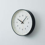 Essent Clock in white and black, featuring clean typeface and elegant design for modern decor.