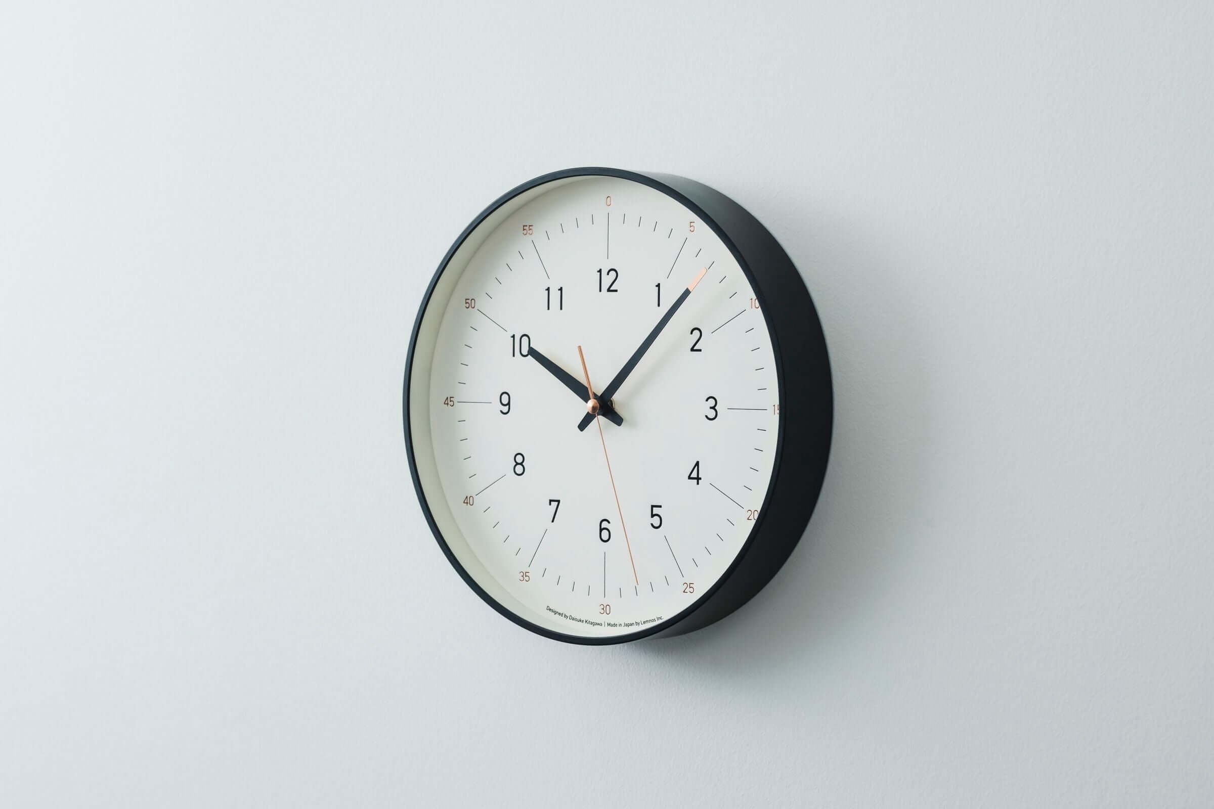 Essent Clock in white and black, featuring clean typeface and elegant design for modern decor.