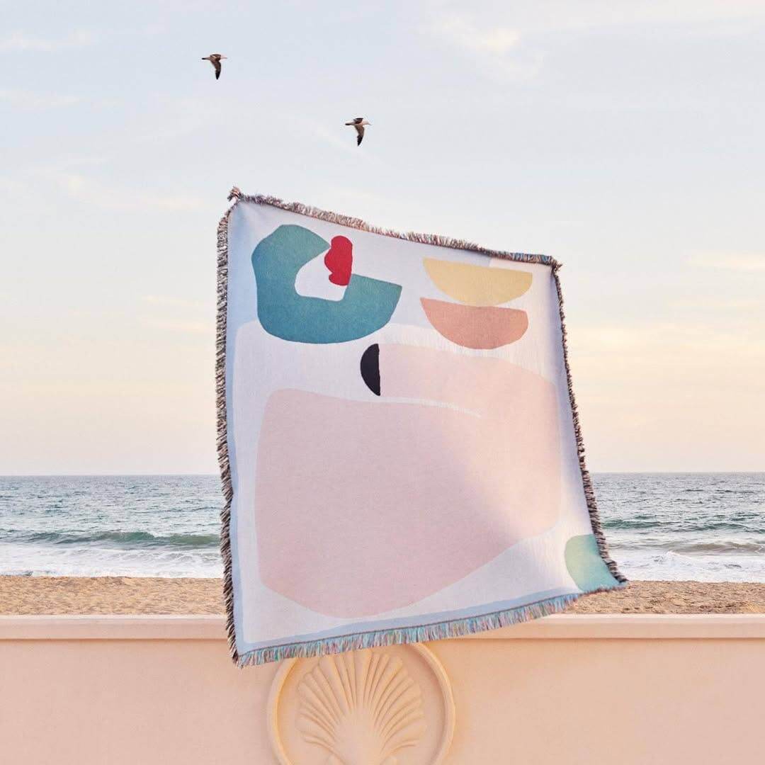 Arthur Throw blanket by Laurie Maun, eco-friendly design on the beach with ocean backdrop.
