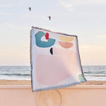 Arthur Throw blanket by Laurie Maun, eco-friendly design on the beach with ocean backdrop.