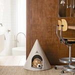 Dog lying in a cone-shaped pet bed in a modern room with wooden walls and a chair.