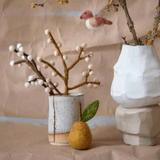 Handmade felt pear ornament with green leaf beside decorative vases and branches for spring home decor.