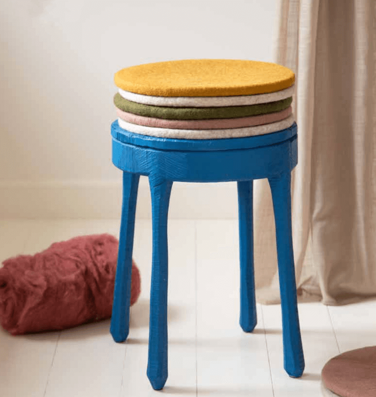 Colorful felt wool seat cushions stacked on a blue stool in a cozy indoor setting.