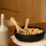Black bowl with salad on a wooden table next to a bottle