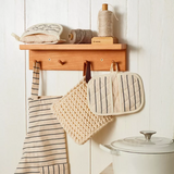 Wooden shelf with kitchen items including an apron, pot holders, and a white pot on a light wooden surface.