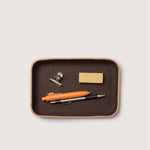 Brown wool and tan leather tray with office supplies including a pen, clip, and business card holder on a light gray background
