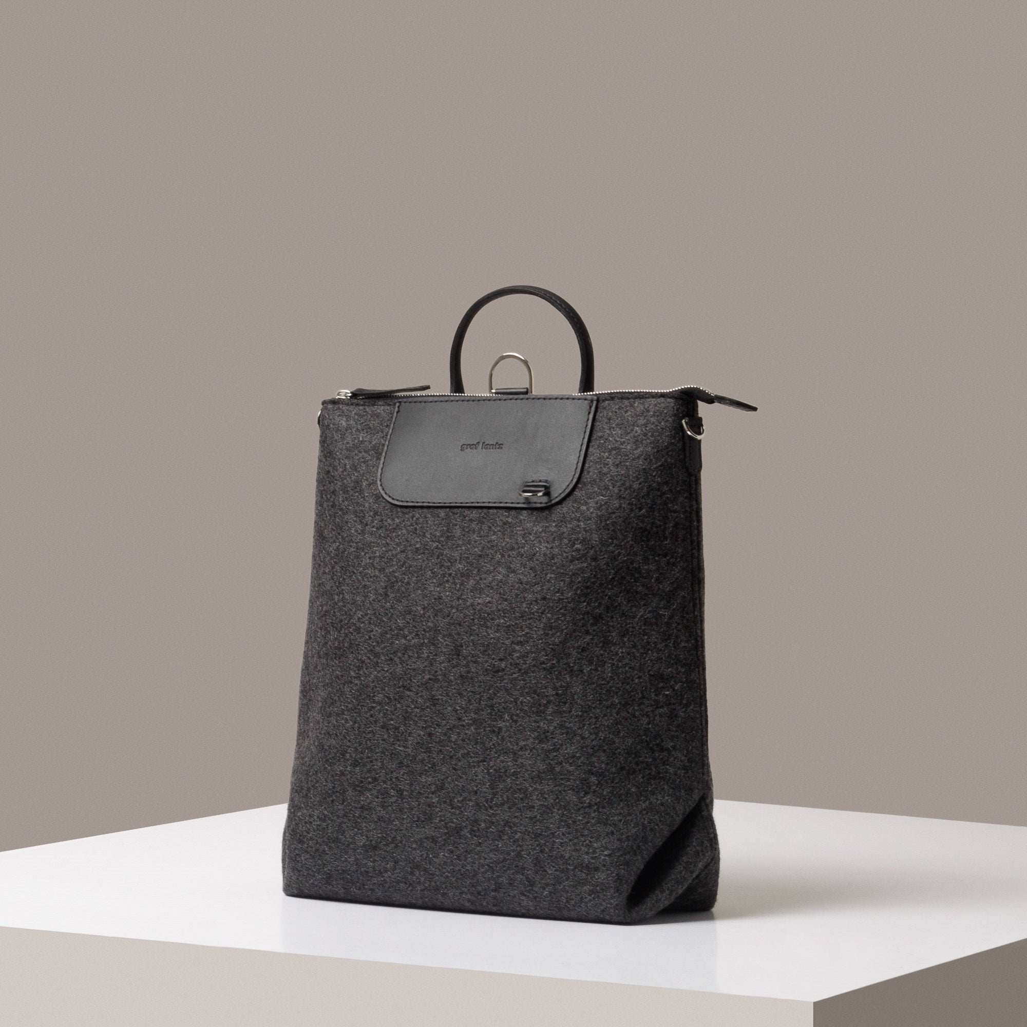 A stylish Bedford Merino Wool Felt Backpack in dark gray, displayed in a three-quarter view on a white base