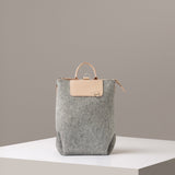 A Bedford Merino Wool Felt Midi Backpack in light grey standing on a white base, front view