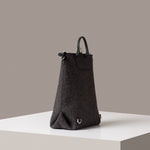 A dark grey Bedford Merino Wool Felt Backpack on a white base displayed in a side-view
