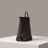 A dark grey Bedford Merino Wool Felt Backpack on a white base displayed in a side-view
