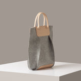A Frankie Merino Wool Felt Tote in a grey color with beige leather accents on a white base displayed in a side-view
