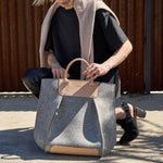 Stylish woman squatting with a granite-colored Frankie Merino Wool Felt Tote bag, demonstrating the bag's design and functionality