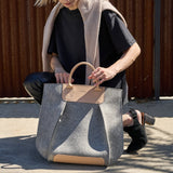 Stylish woman squatting with a granite-colored Frankie Merino Wool Felt Tote bag, demonstrating the bag's design and functionality