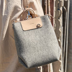 A Bedford Merino Wool Felt Midi Backpack carried by a woman over her shoulder, showcasing its light grey and beige colors