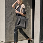 A woman carries a charcoal-colored Frankie Merino Wool Felt tote bag over her arm while walking, showcasing its chic design