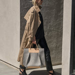 A Frankie Merino Wool Felt Tote carried by a woman, showcasing its handle-lengths and beige and grey colors