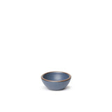 A tiny rounded ceramic bowl in a cool medium blue color featuring iron speckles and an unglazed rim