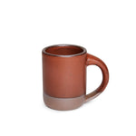 A medium sized ceramic mug with handle in a cool burnt terracotta color featuring iron speckles and unglazed rim and bottom base.