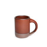 A medium sized ceramic mug with handle in a cool burnt terracotta color featuring iron speckles and unglazed rim and bottom base.