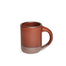 A medium sized ceramic mug with handle in a cool burnt terracotta color featuring iron speckles and unglazed rim and bottom base.