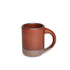 A medium sized ceramic mug with handle in a cool burnt terracotta color featuring iron speckles and unglazed rim and bottom base.
