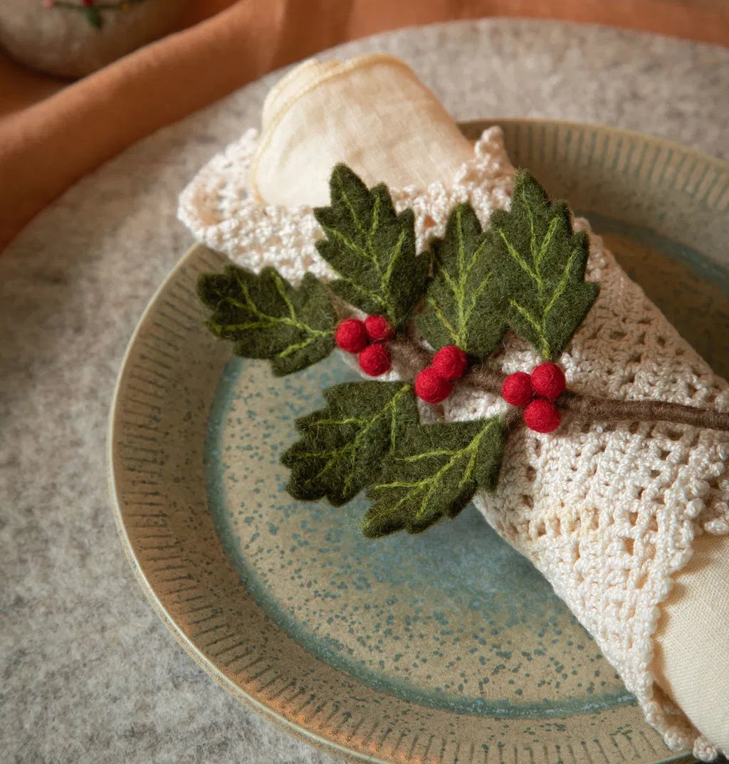 Decorative plate with a crocheted napkin and holly leaves on a textured surface.
