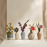 Five small ceramic vases with floral arrangements on a neutral background