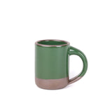 A medium sized ceramic mug with handle in a glossy emerald green color featuring iron speckles and unglazed rim and bottom base.