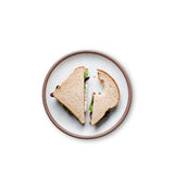 A sandwich on a medium sized ceramic plate in a cool white color featuring iron speckles and an unglazed rim.