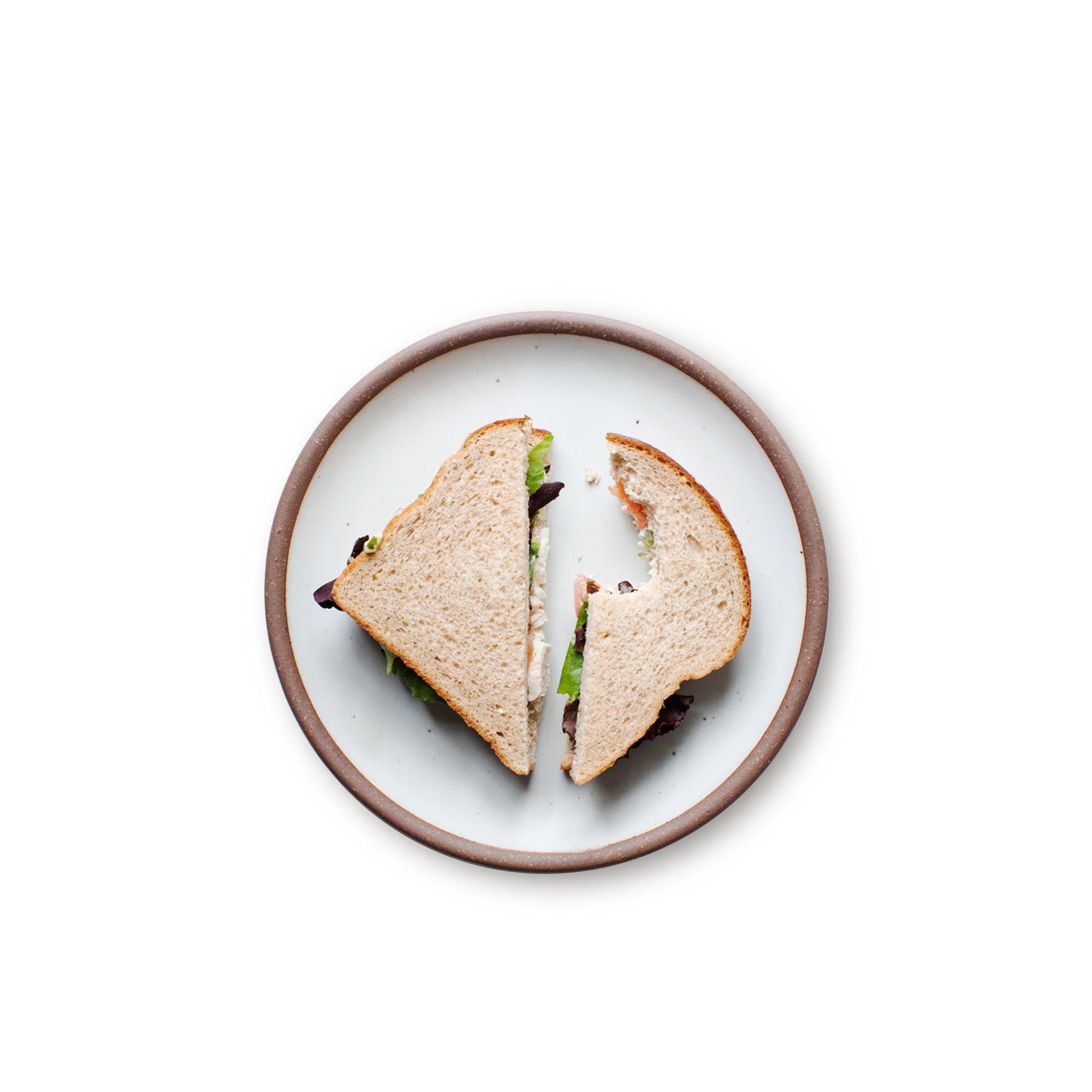 A sandwich on a medium sized ceramic plate in a cool white color featuring iron speckles and an unglazed rim.