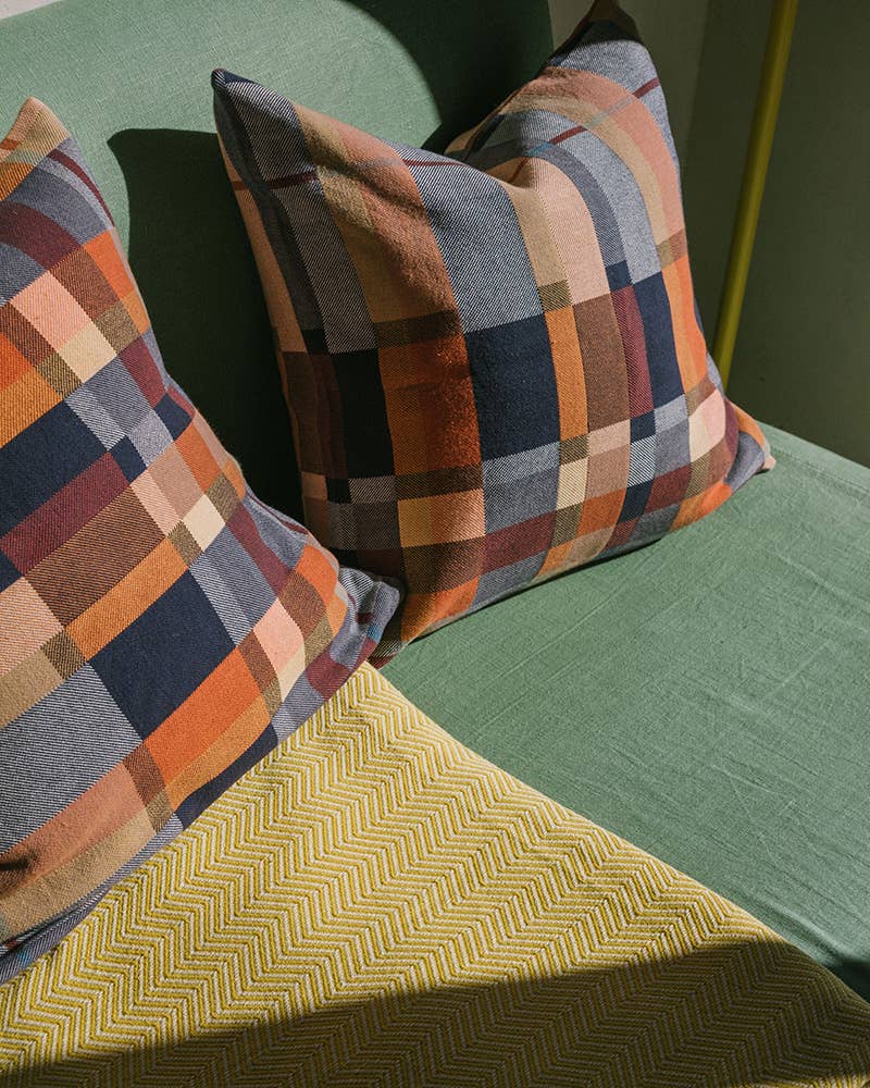 Plaid patterned pillows on a green sofa next to yellow throw. 