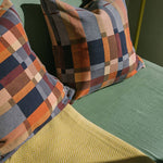 Plaid patterned pillows on a green sofa next to yellow throw. 