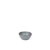 A tiny rounded ceramic bowl in a blue-grey color featuring iron speckles and an unglazed rim