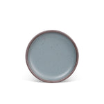 A medium sized ceramic plate in a blue-grey color featuring iron speckles and an unglazed rim.
