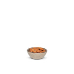 A tiny rounded ceramic bowl in a warm pale brown color featuring iron speckles and an unglazed rim, filled with almonds