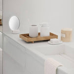 Bathroom counter with white containers, a wooden tray, and a small round mirror.