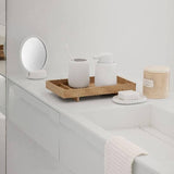 Bathroom counter with white containers, a wooden tray, and a small round mirror.