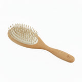 A wooden hairbrush with a light natural wood handle and head, beige bristles, and a white inner pad, shown on a plain white background.