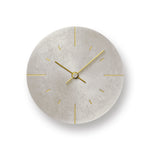 A minimalist round wall clock with a textured light silver colored face and slim gold hands, hour markers, and central hub, shown against a white background with a soft drop shadow.
