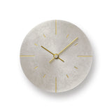 A minimalist round wall clock with a textured light silver colored face and slim gold hands, hour markers, and central hub, shown against a white background with a soft drop shadow.