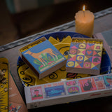 Matches boxes with colorful designs on a table with a lit candle in the background