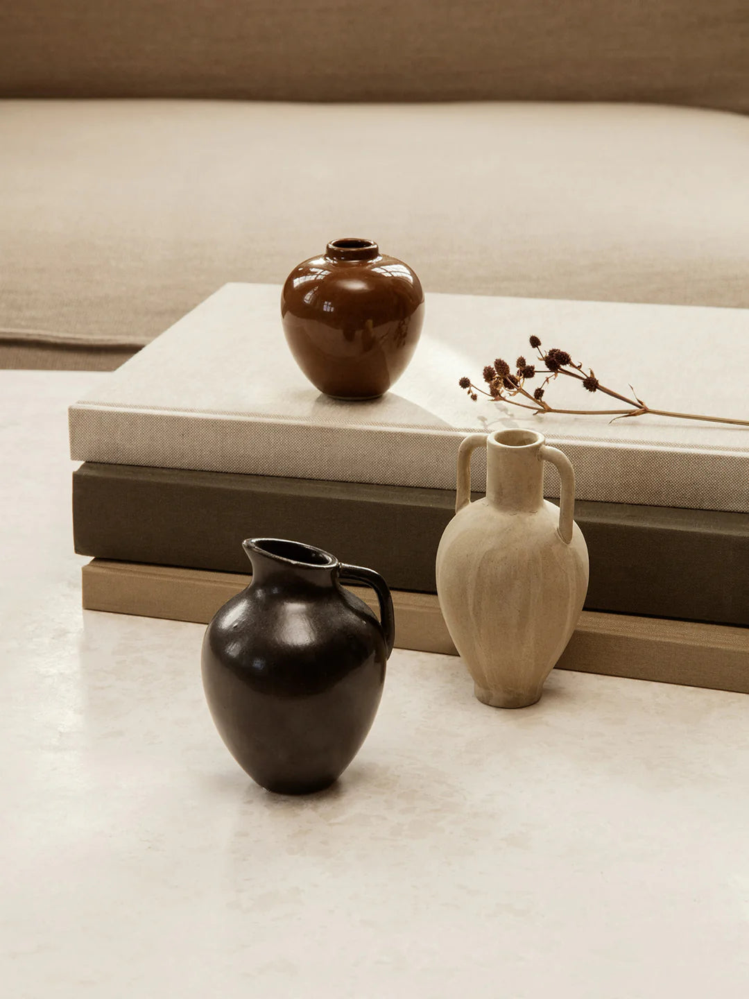 A petite, ceramic Ary Mini Vase in charcoal color, displayed alongside other vases on a neutral background.