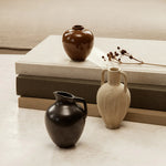 A petite, ceramic Ary Mini Vase in charcoal color, displayed alongside other vases on a neutral background.