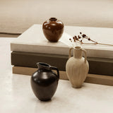 A petite, ceramic Ary Mini Vase in charcoal color, displayed alongside other vases on a neutral background.