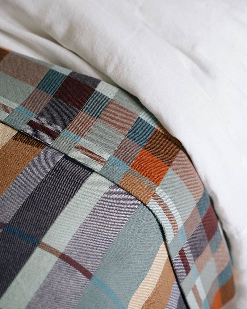 Close-up of a plaid fabric with brown, blue, and beige colors on a white background.