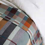 Close-up of a plaid fabric with brown, blue, and beige colors on a white background.