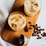 Two glasses of iced coffee with coffee beans on a wooden board.