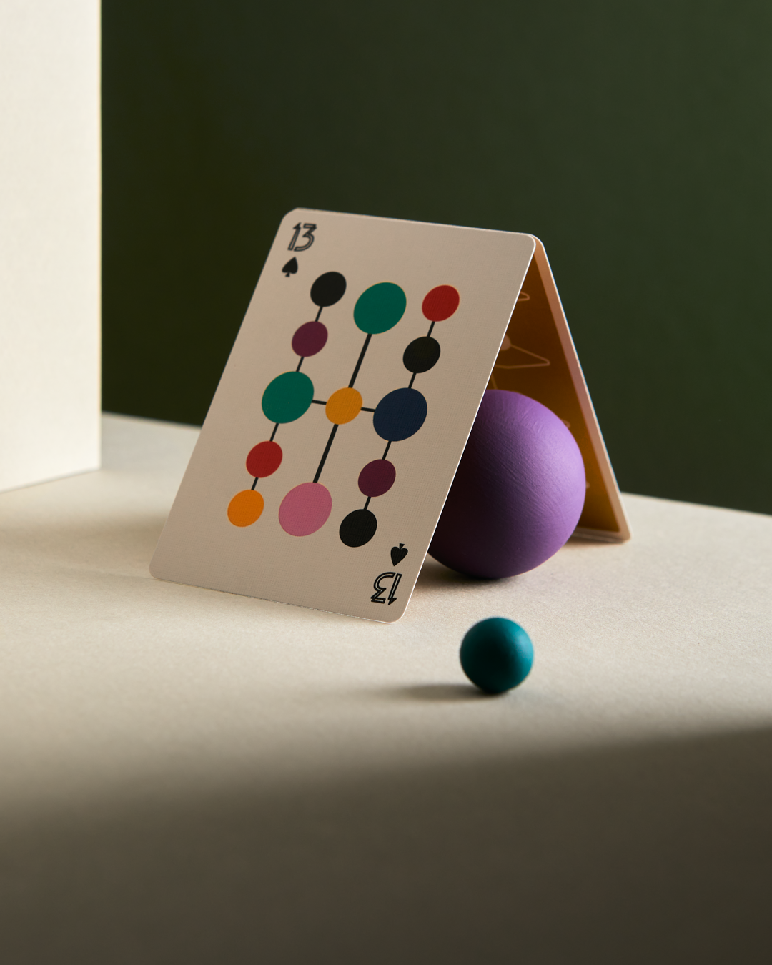 Playing card with colorful design on a table with a purple ball and blue sphere.