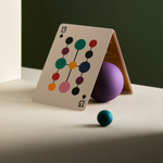 Playing card with colorful design on a table with a purple ball and blue sphere.
