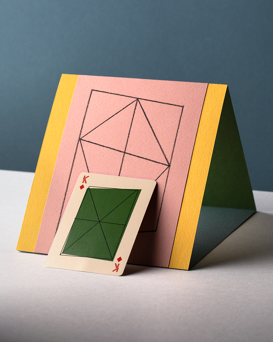 King of Diamonds playing card with green geometric shape laying against kite shaped geometric illustration against blue background